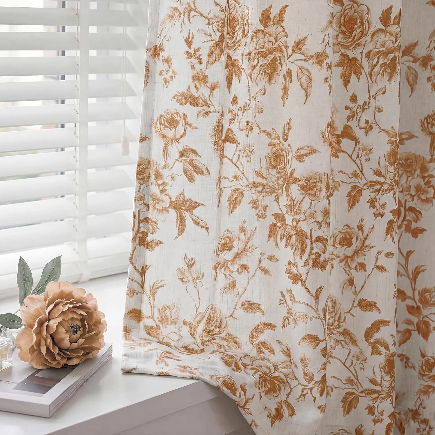 Beige sheer linen curtain with brown floral print beside white window blinds