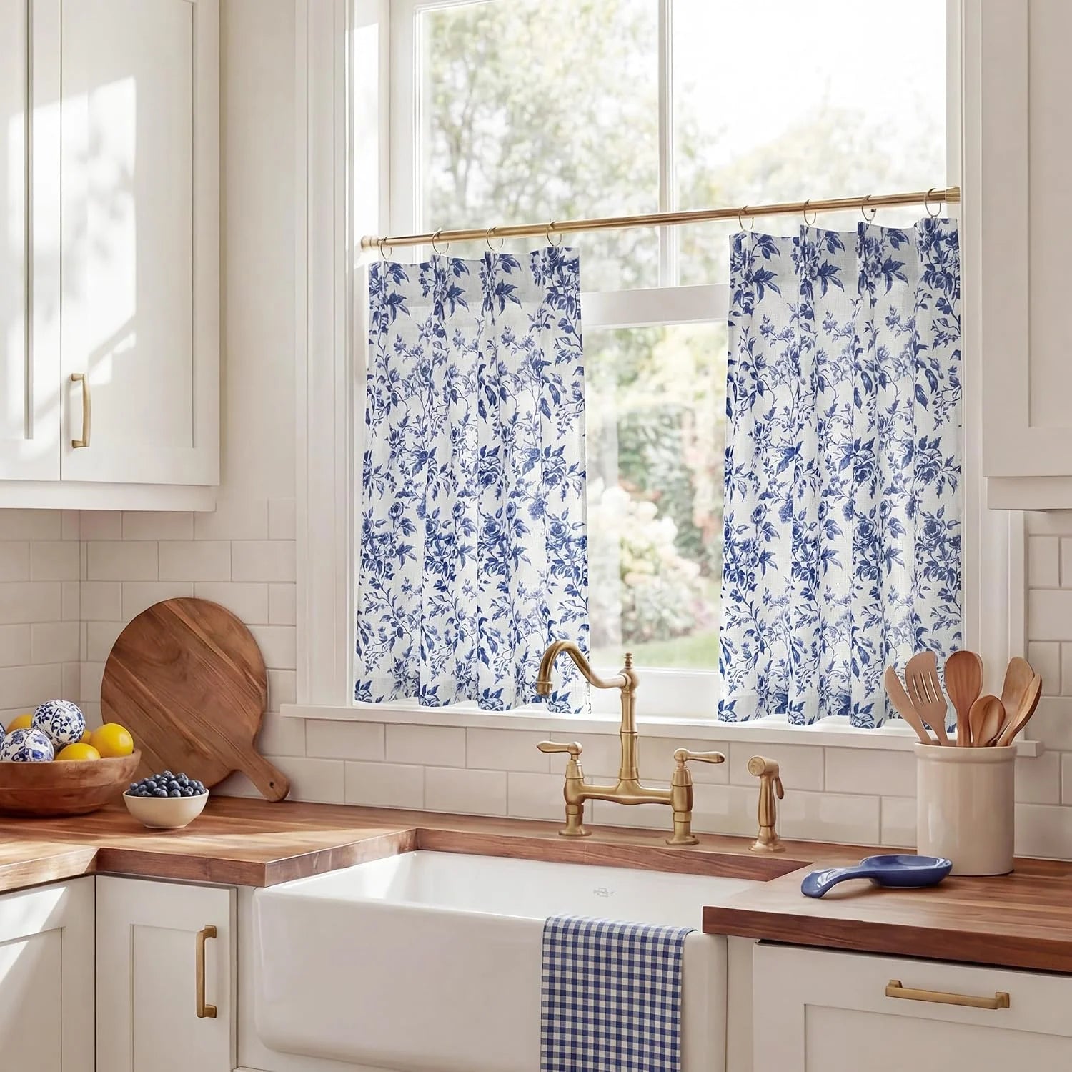 Blue floral cafe curtains hanging on a brass rod above a bright farmhouse kitchen sink