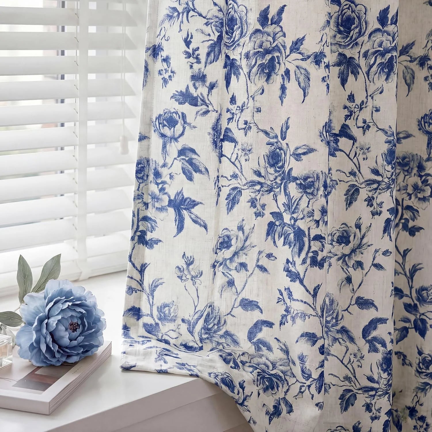Blue floral linen curtain panel beside white blinds on a bright window sill