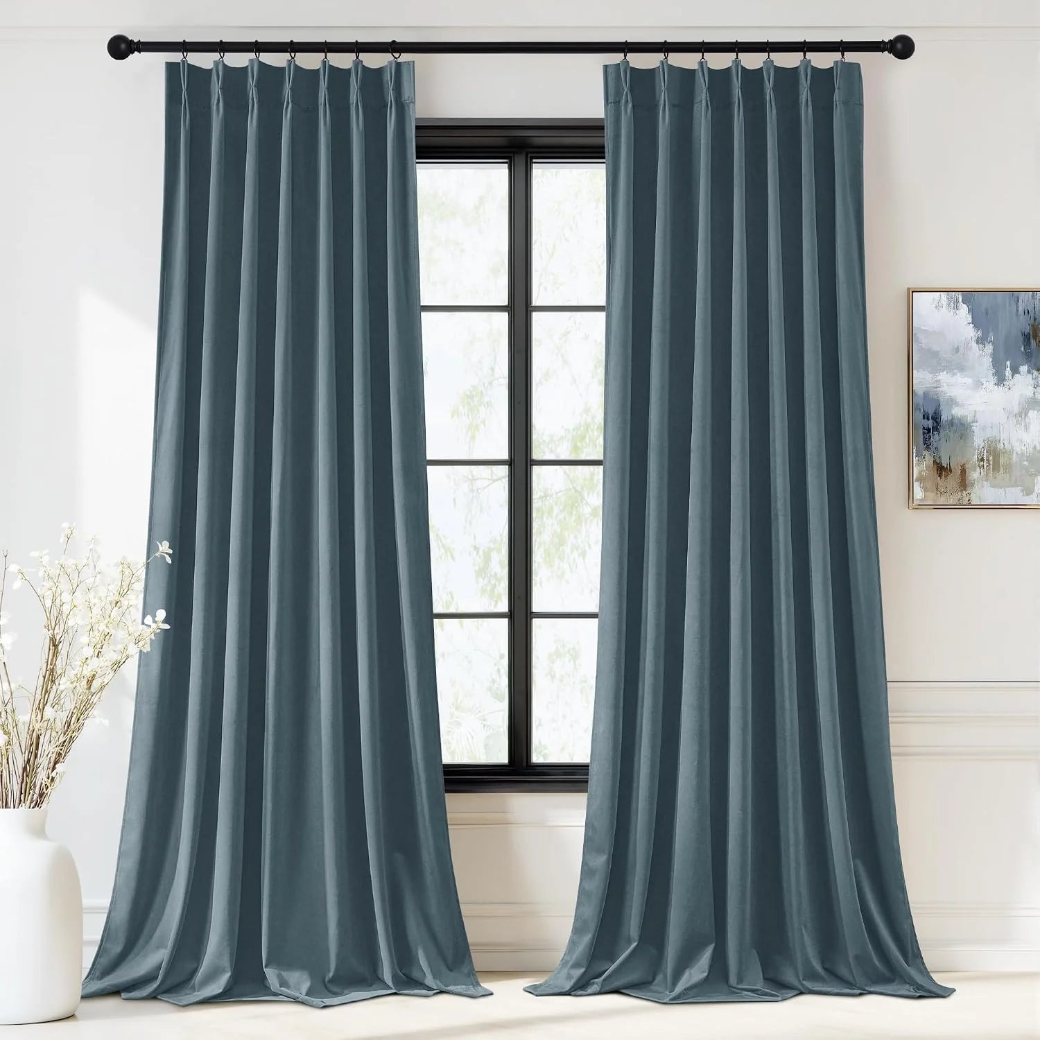 Blue gray pinched pleat curtains hanging on a black rod in a bright modern room
