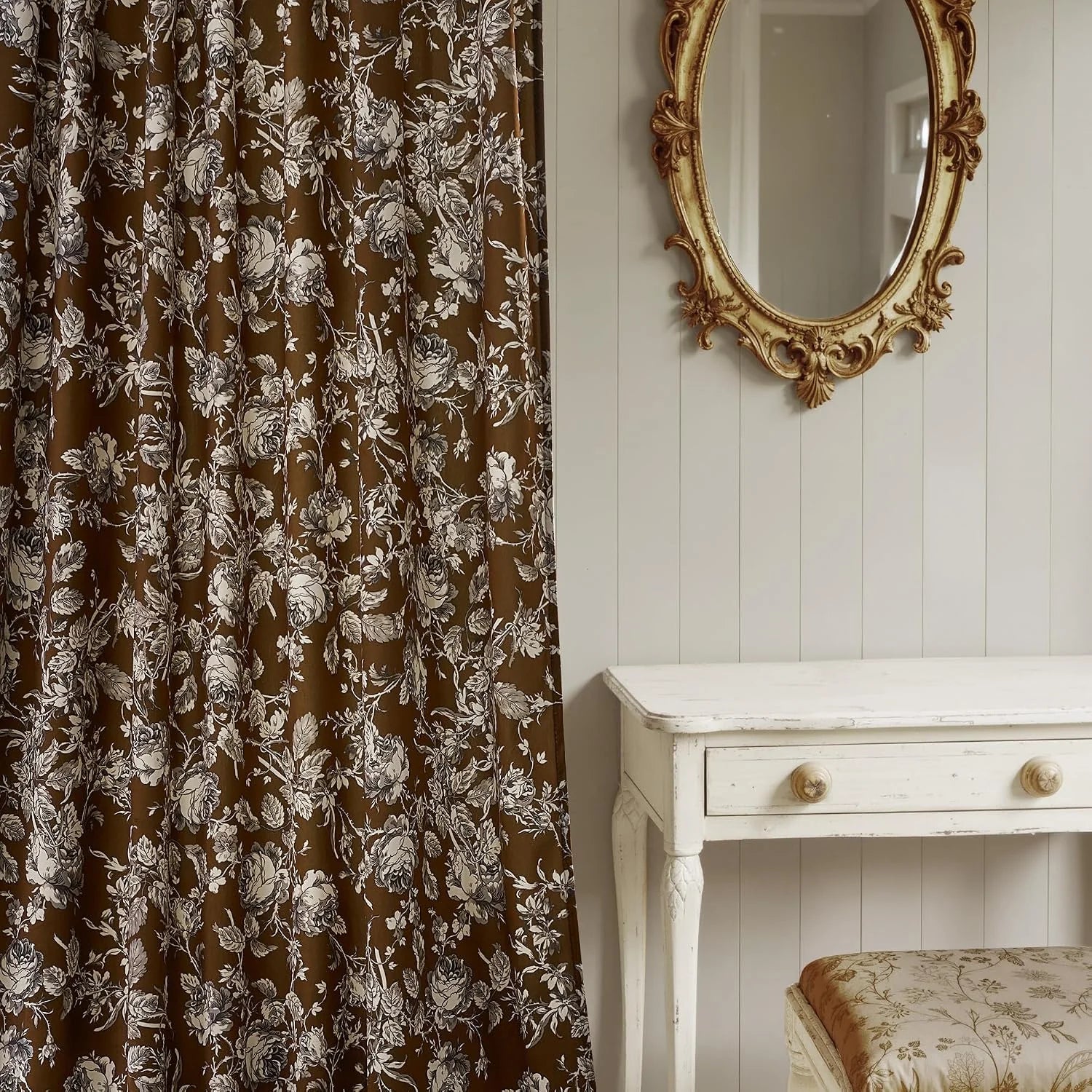 Brown floral curtain panel beside a distressed white vanity and ornate gold mirror