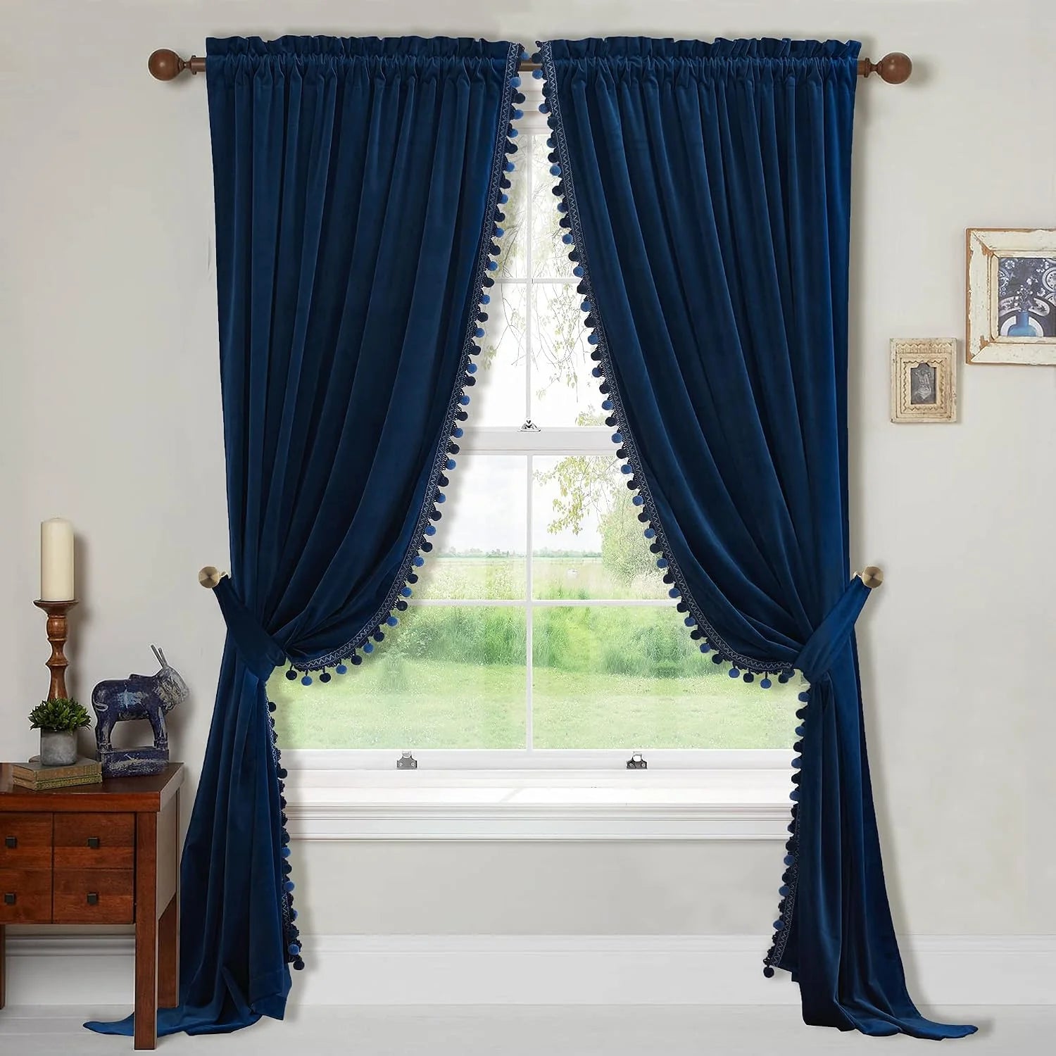 Navy velvet curtains with pom-pom trim tied back on a wooden rod over a bright window