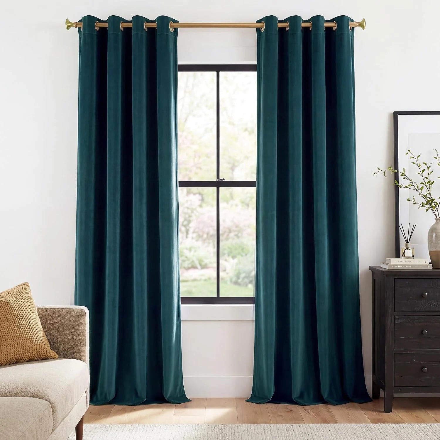 Dark teal velvet curtains with gold grommets hanging on a brass rod by a window
