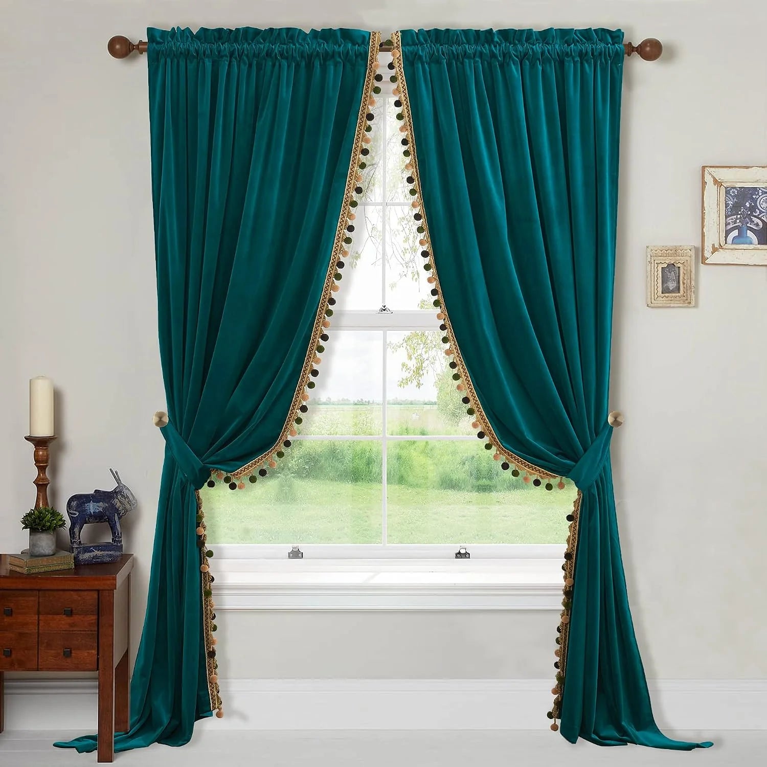 Teal velvet curtains with pom pom trim and tiebacks framing a bright window